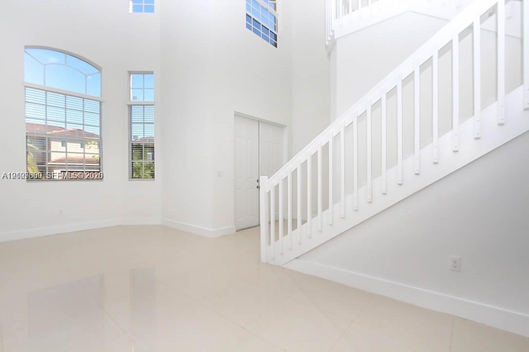 Double-height ceiling, large arched window, polished tile flooring, white wood staircase railing, and double-door entry