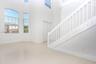 Double-height ceiling, large arched window, polished tile flooring, white wood staircase railing, and double-door entry