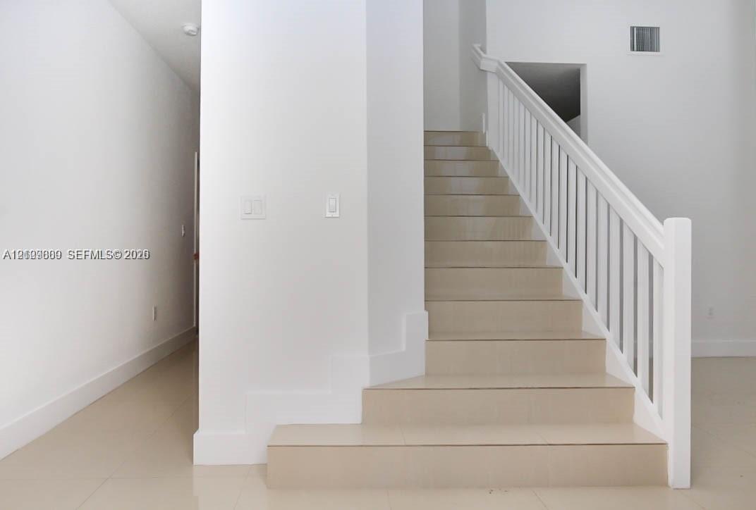 Staircase featuring tile treads and a white wooden handrail with vertical balusters