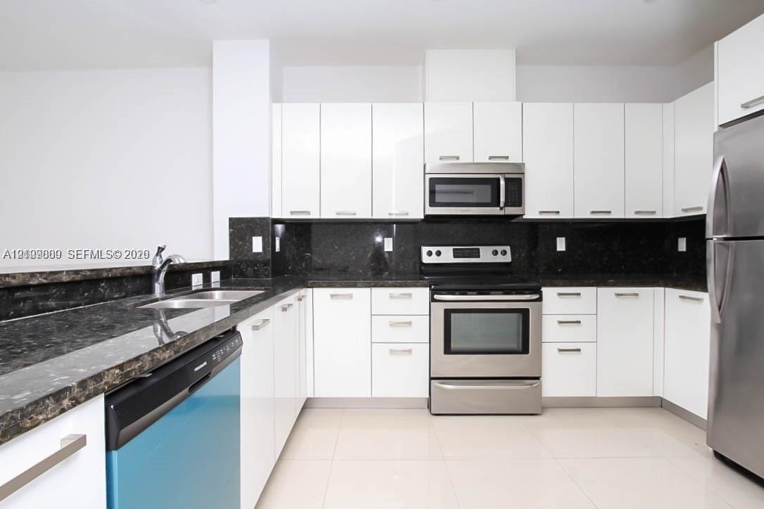 Kitchen featuring white flat-panel cabinetry, dark stone countertops, tile flooring, and a stainless steel appliance suite