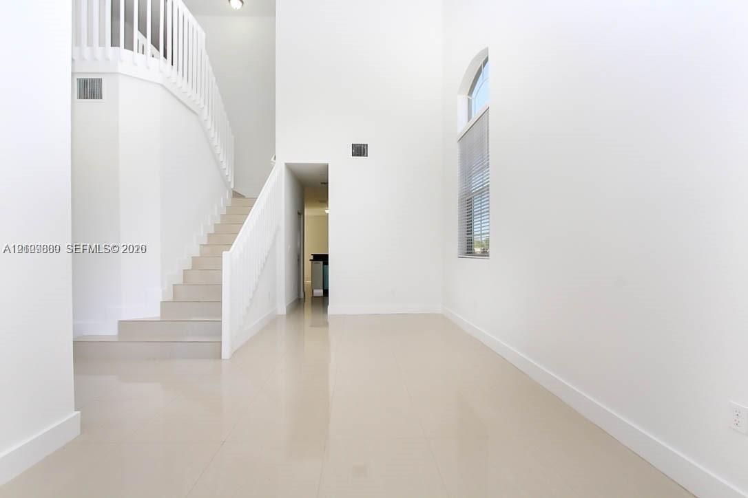 Double-height ceilings featuring an arched window, large-format tile flooring, and a white staircase with a matching balustrade