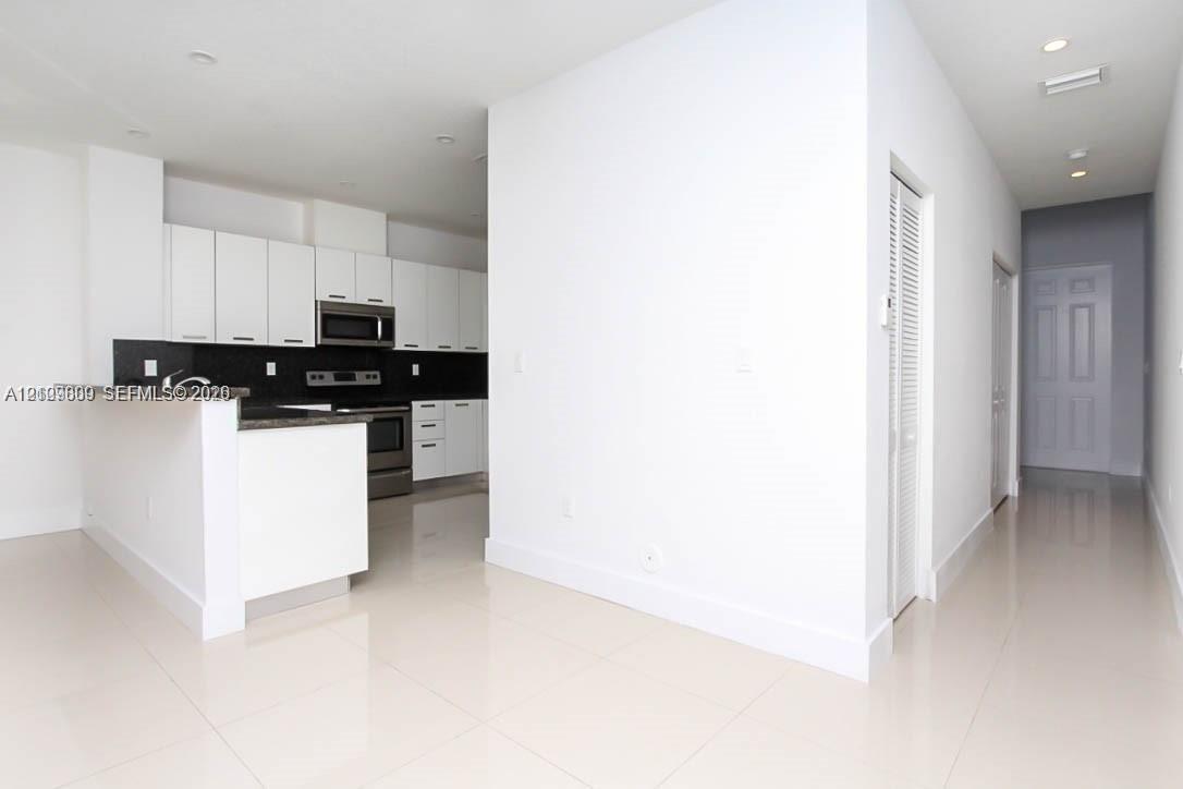 Kitchen featuring white flat-panel cabinetry, dark stone countertops, stainless steel appliances, and tile flooring