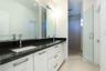 Dual-sink vanity featuring stone countertops, white cabinetry with horizontal hardware, two wall-mounted mirrors, and a glass-enclosed shower