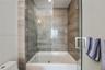 Shower-tub combination featuring floor-to-ceiling stone-tile surround, frameless glass panel, and polished chrome fixtures