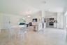 Open floor plan featuring vaulted ceilings, neutral large-format tile flooring, a kitchen island with white cabinetry, stainless steel appliances, and