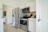 Kitchen featuring white shaker-style cabinetry, stainless steel appliances, brushed gold-tone hardware, a tiled backsplash, and stone-finish counterto