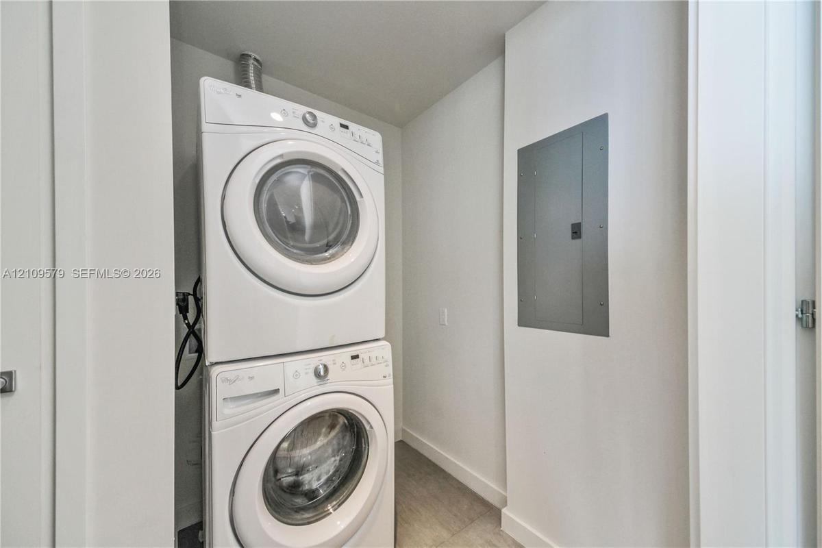 Dedicated laundry area featuring a stacked washer and dryer set and a recessed electrical service panel