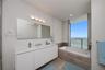 Double vanity with integrated sinks, frameless wall-to-wall mirror, built-in soaking tub with stone-finish surround, wood-finish flooring, and floor-t