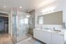 Dual-sink vanity with white cabinetry and rectangular basins, oversized frameless vanity mirror, glass-enclosed walk-in shower with tiled walls and ra