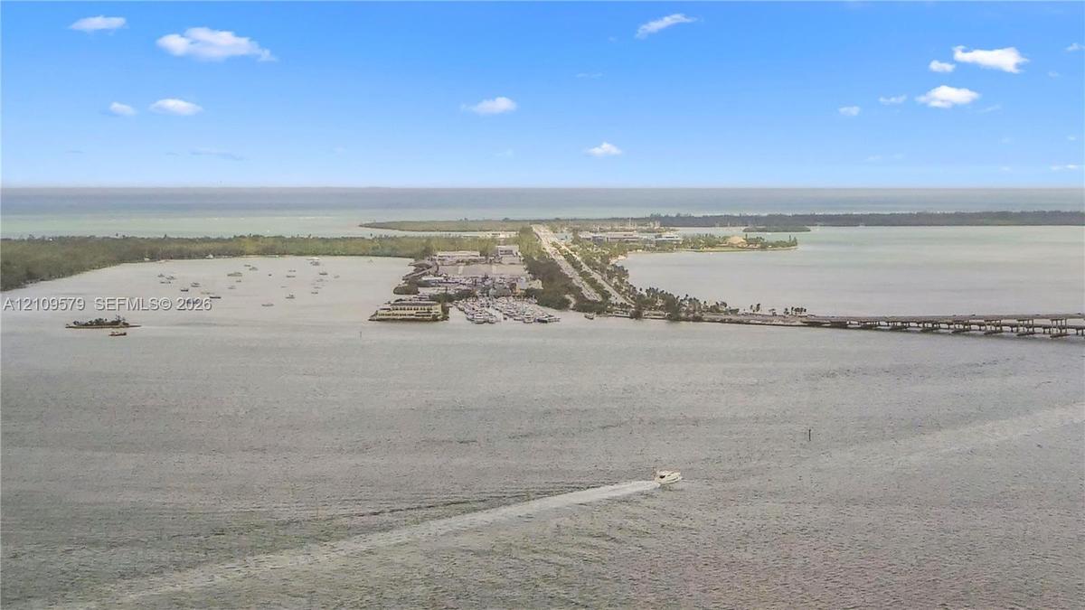 Aerial perspective of coastal landscape featuring expansive open water, a bridge, and a land-based thoroughfare