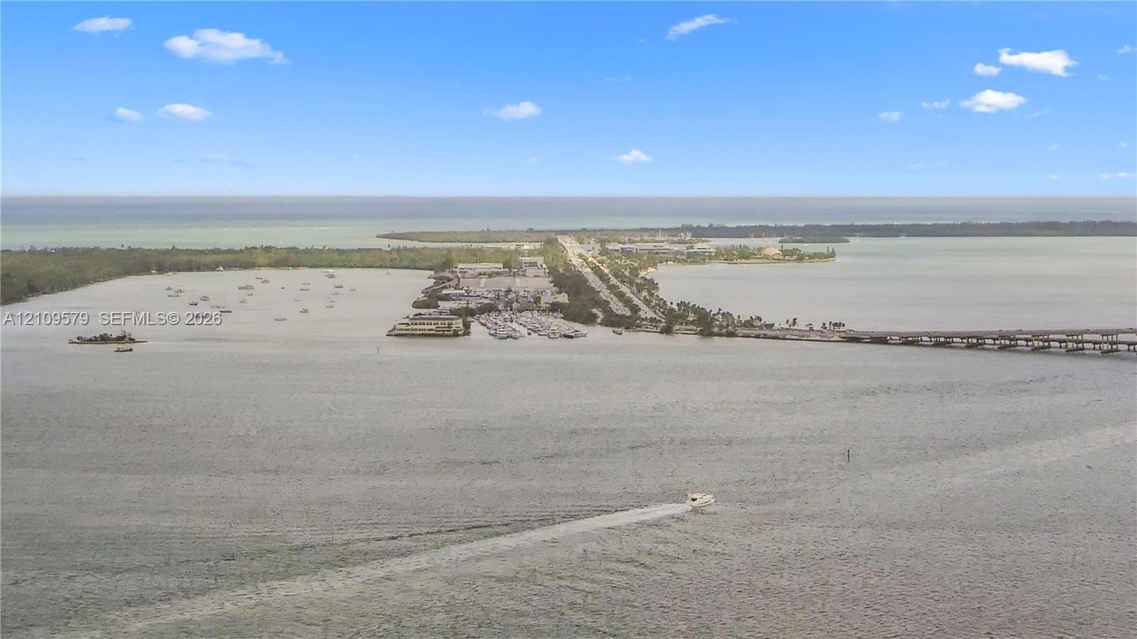 Aerial perspective of coastal landscape featuring expansive open water, a bridge, and a land-based thoroughfare