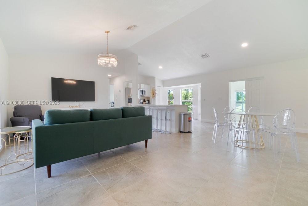 Open-concept interior featuring vaulted ceilings, oversized tile flooring, a tiered kitchen island with bar seating, and a decorative tiered chandelie