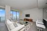 Living area featuring floor-to-ceiling glass sliding doors, private balcony with metal railing, large-format tile flooring, and integrated recessed li