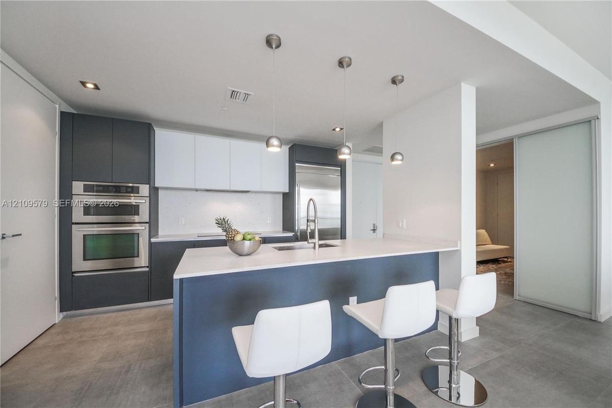 Modern kitchen featuring matte charcoal and white cabinetry, quartz countertops, stainless steel built-in double wall oven, central island with under-