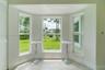Bay window with triple-pane windows, neutral stone-finish tile flooring, and white louvered closet doors