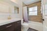 Bathroom featuring a vanity with wood-finish cabinetry, a white integrated countertop, brass-tone faucet, large wall-mounted mirror, and a tub-shower 