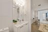 Bathroom vanity with a stone countertop, integrated basin, brushed metal hardware, and an expansive wall-mounted mirror with multi-light fixture