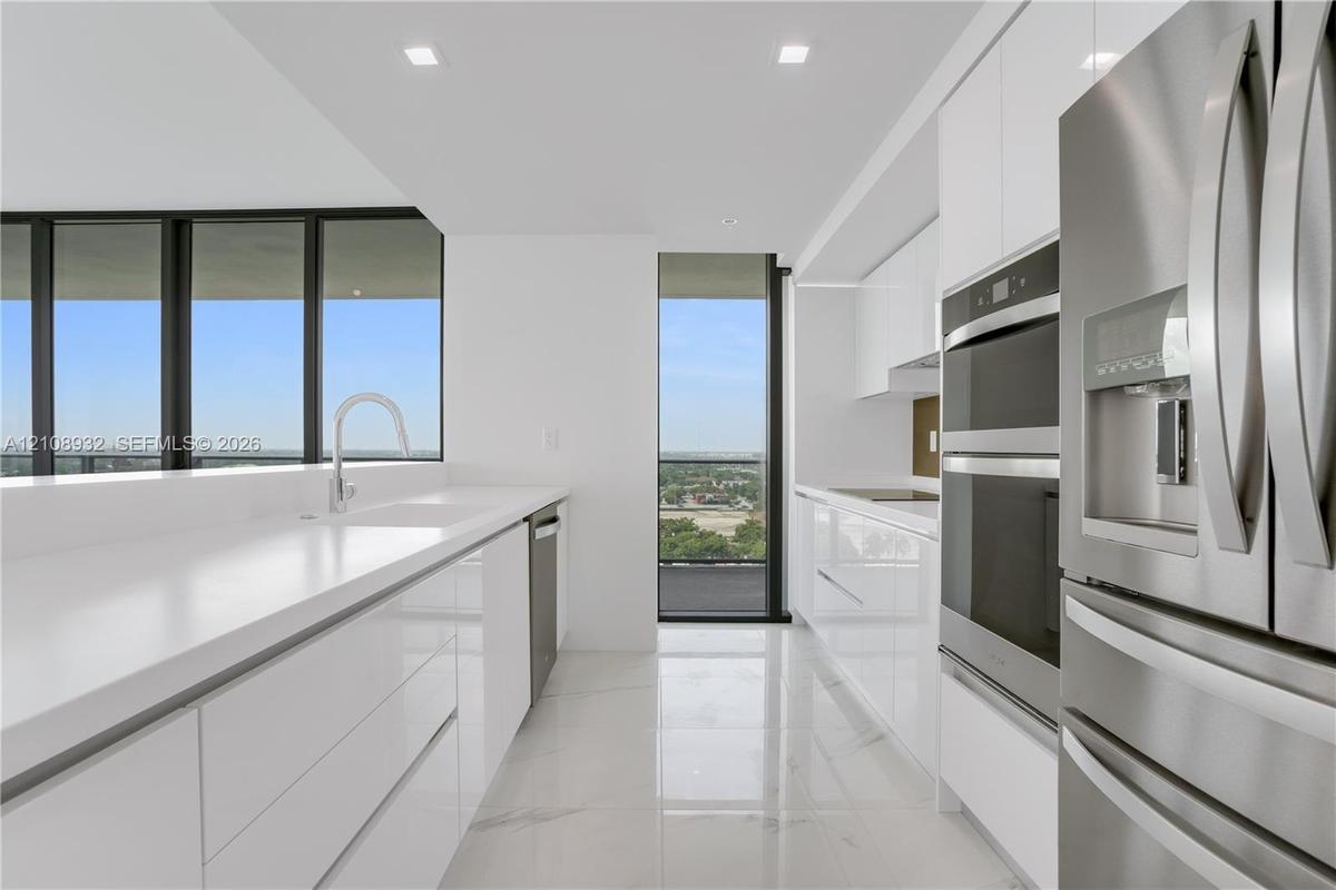 Kitchen featuring white gloss cabinetry, expansive solid-surface countertops, stainless steel double wall ovens, high-gloss tile flooring, and floor-t