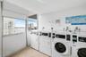 Laundry room featuring ceramic tile flooring, floor-to-ceiling windows, and multiple commercial-grade front-loading washing machines and dryers