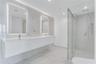 Floating dual vanity with integrated sinks, back-lit mirrors, walk-in glass shower enclosure, and full-height stone-finish wall tiling