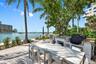 Waterfront patio featuring stone-tiled flooring, a built-in outdoor kitchen with stone countertops and a stainless-steel grill, and mature palm trees