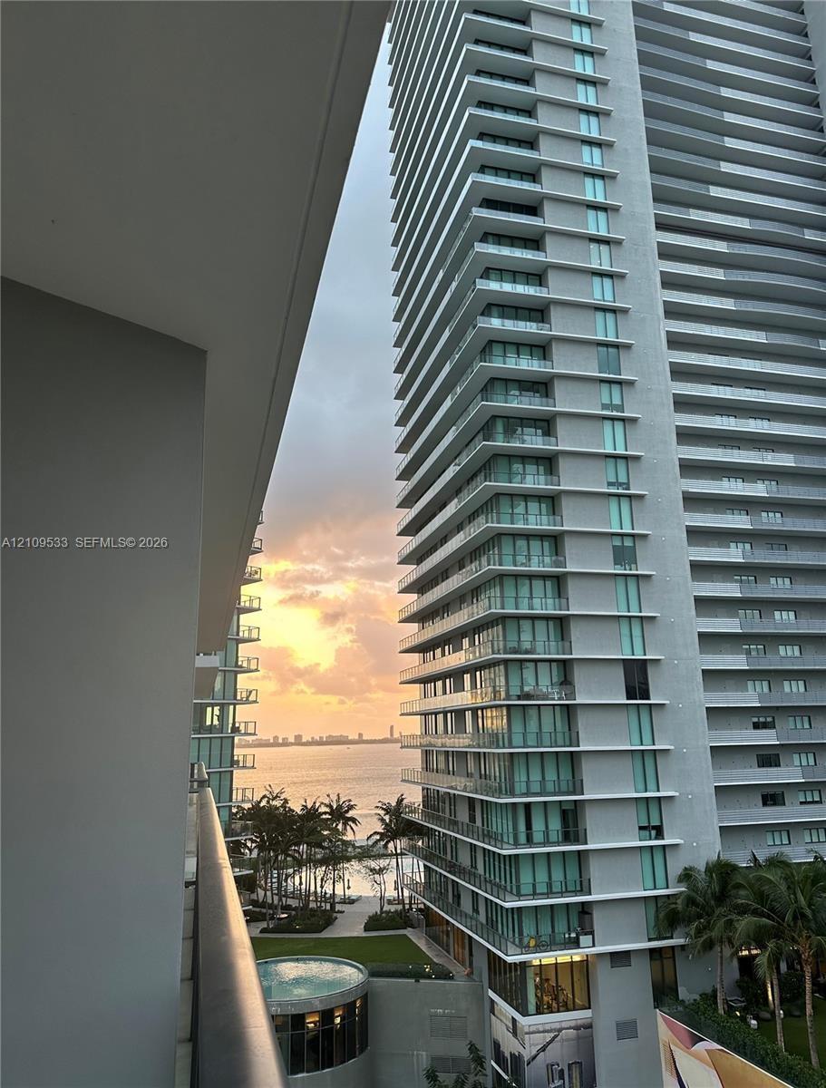 High-rise balcony featuring glass railings and panoramic water, skyline, and sunset scenery