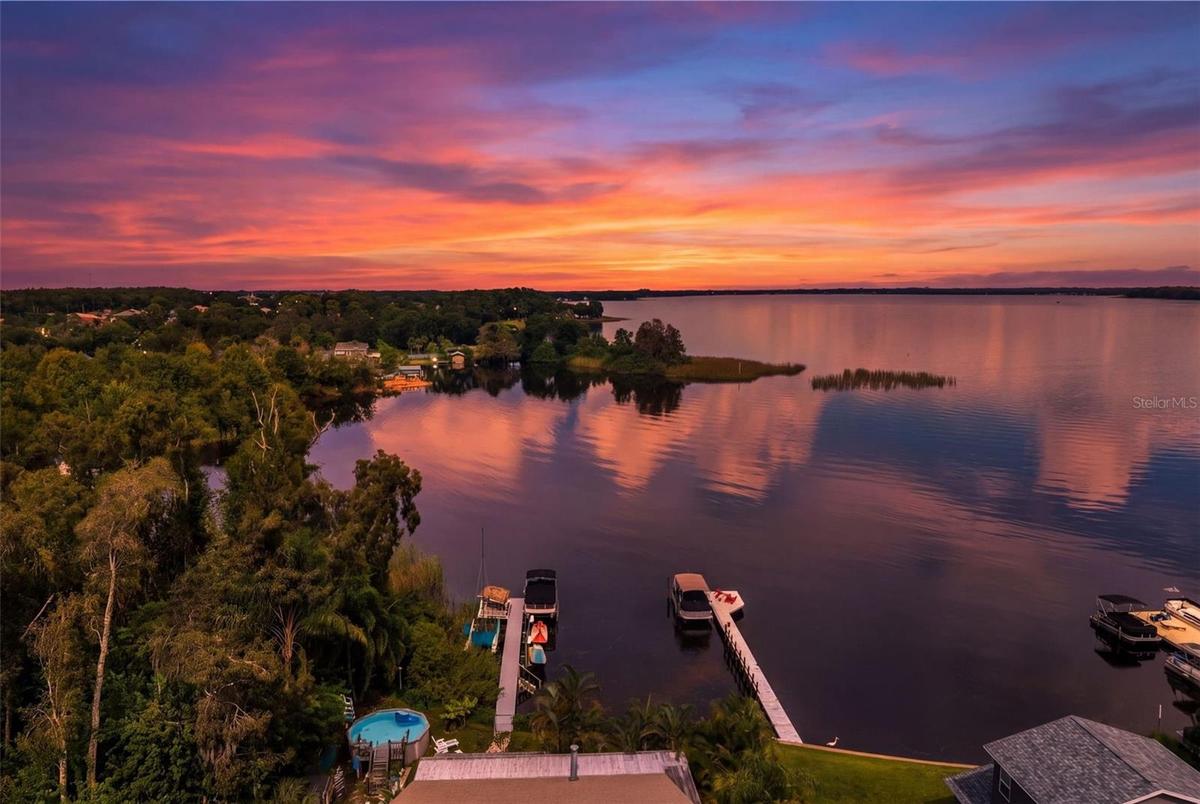 An incredible aerial perspective showcases the property's waterfront setting, private dock, and sweeping views across the water. With vibrant sunrise 