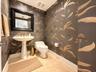 Powder room featuring floral-patterned wallpaper, a white pedestal sink with a brass-finish faucet, a one-piece toilet, and large-format tile flooring