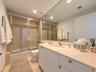 Full-width vanity with a stone countertop and integrated oval sink, floor-to-ceiling mirror, and shower-tub combination with a glass sliding enclosure