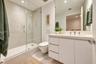 Bathroom featuring a white vanity with an integrated countertop, wall-mounted toilet, walk-in shower with a glass enclosure, and light-toned tile floo