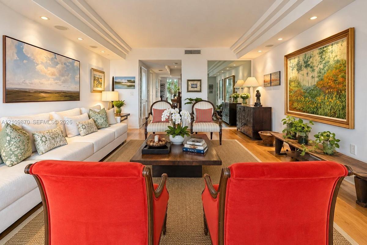 Living space featuring recessed lighting, multi-layered crown molding, mirror-paneled accent walls, and wood-finish flooring