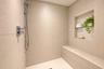 Walk-in shower featuring textured wall tile, a built-in stone bench, a recessed wall niche with glass shelving, and a multi-function handheld shower h