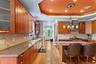 Kitchen with light wood finished floors, a tray ceiling, ornamental molding, wall chimney exhaust hood, and brown cabinets