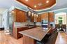 Kitchen with appliances with stainless steel finishes, a chandelier, crown molding, brown cabinetry, and wall chimney range hood
