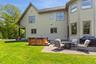 Back of house with a hot tub, a patio, a yard, an outdoor fire pit, and a shingled roof