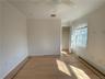 Unfurnished bedroom featuring a closet, baseboard heating, ceiling fan, wood-type flooring, and ornamental molding