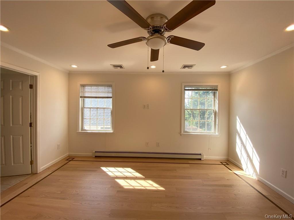 Empty room with a baseboard radiator, ceiling fan, light wood-type flooring, and crown molding