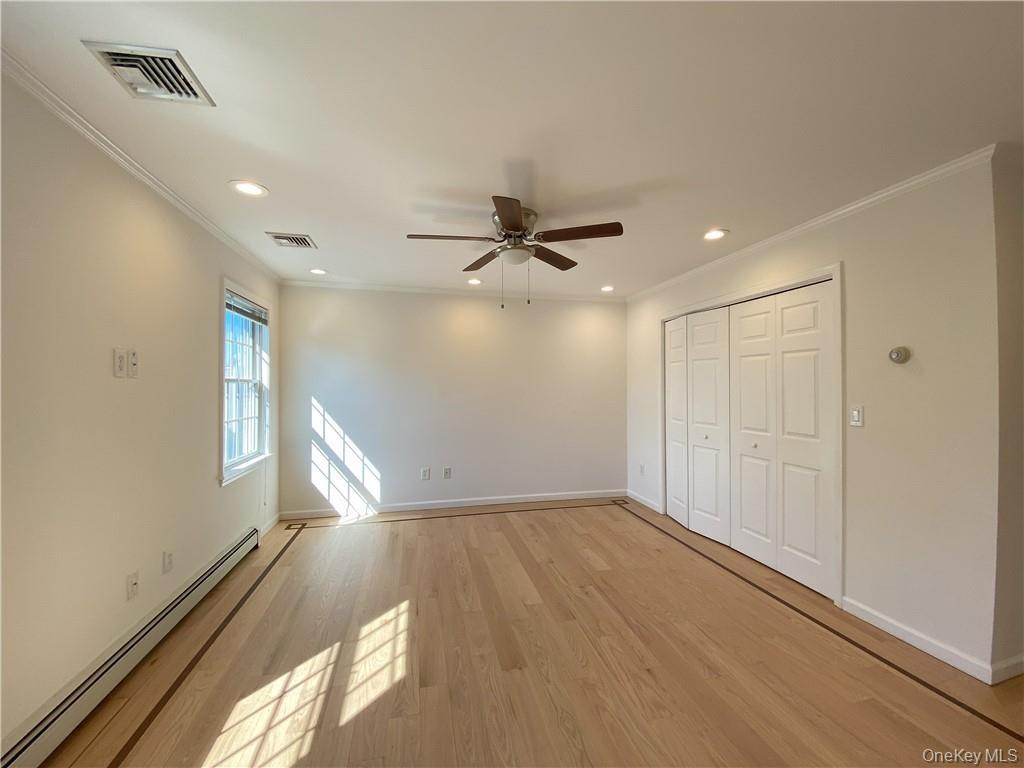 Unfurnished bedroom featuring light hardwood / wood-style flooring, baseboard heating, ceiling fan, and crown molding