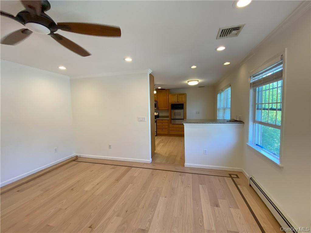 Unfurnished living room with baseboard heating, ceiling fan, light wood-type flooring, and crown molding
