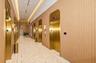 Elevator lobby featuring metallic gold-finish doors, wood-paneled walls, recessed ceiling lighting, and polished stone tile flooring