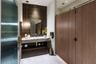 Floating vanity with a stone countertop, vertical tile backsplash, gold-tone pendant lighting, irregular-shaped mirror, and wood-finish partition door