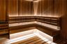 Custom cedar-paneled sauna featuring tiered L-shaped benches, integrated linear accent lighting, and a wall-mounted heater unit