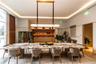 Custom stone-topped table, linear suspended light fixture, recessed tray ceiling with integrated cove lighting, and built-in cabinetry with stone-fini
