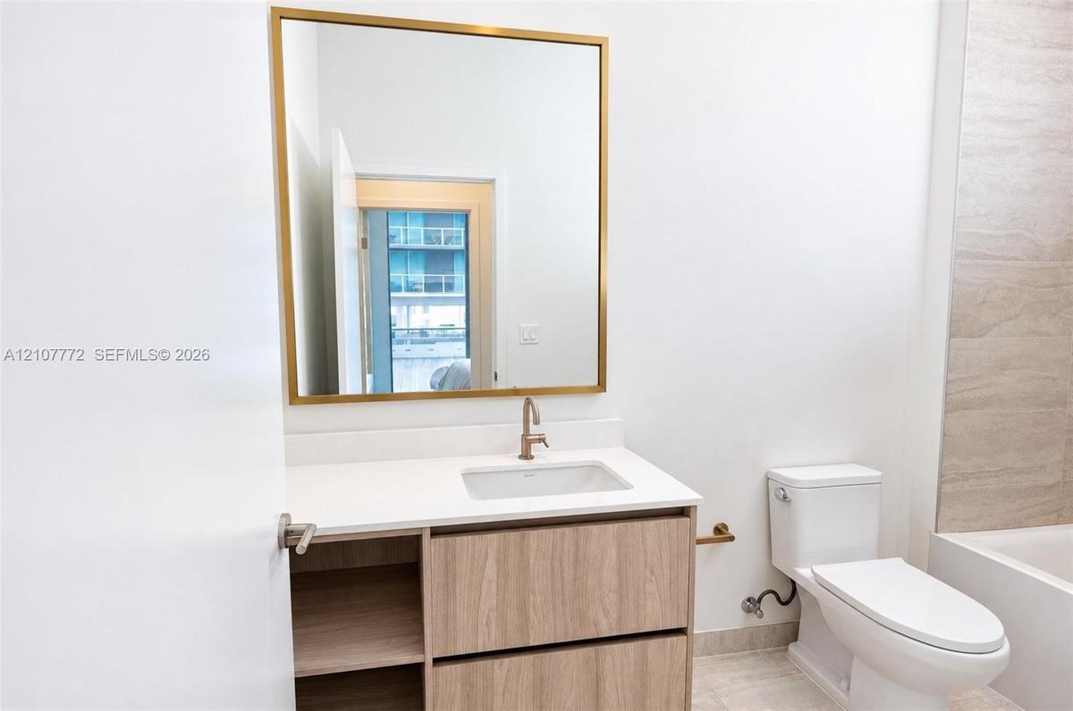 Bathroom featuring a vanity with wood-finish cabinetry, white countertop with an integrated basin, gold-toned hardware, and a square wall mirror with 