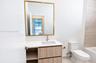 Bathroom featuring a vanity with wood-finish cabinetry, white countertop with an integrated basin, gold-toned hardware, and a square wall mirror with 