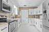 Kitchen featuring white cabinetry with matte black hardware, stainless steel appliances, a metallic mosaic tile backsplash, and gloss-finish floor til