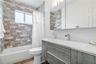 Textured stone tile wall encompassing the bathtub, wood-finish floating vanity, integrated rectangular sink, wall-mounted faucet, and mirrored medicin