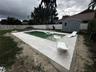 Backyard featuring an in-ground swimming pool with a tanning ledge, light-toned stone-finish paver decking, a white vinyl privacy fence, and a detache