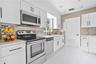 Kitchen featuring white Shaker-style cabinetry, stainless steel appliances, a metallic mosaic tile backsplash, matte black hardware, and tile flooring