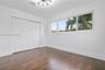 Room featuring dark-toned wood-finish flooring, a multi-arm modern light fixture, expansive horizontal window, and floor-to-ceiling built-in closet wi